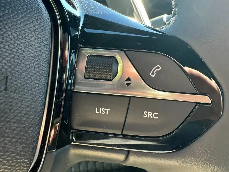 Gros plan sur les commandes au volant noir du Peugeot 2008 1.2 Hybrid 145ch Allure, boutons LIST, SRC et téléphone.