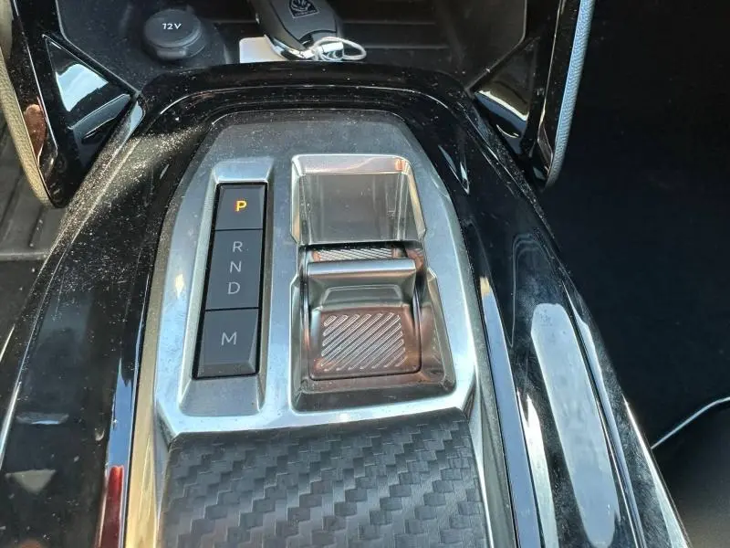 Gros plan sur la console centrale noire brillante du Peugeot 2008 Hybrid 2025, avec levier de vitesses électronique et boutons P, R, N, D, M.