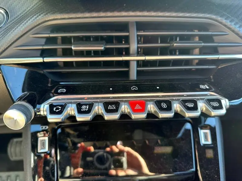 Gros plan sur la console centrale du Peugeot 2008 1.2 Hybrid 145ch Allure 2025, boutons argentés et écran tactile noir.