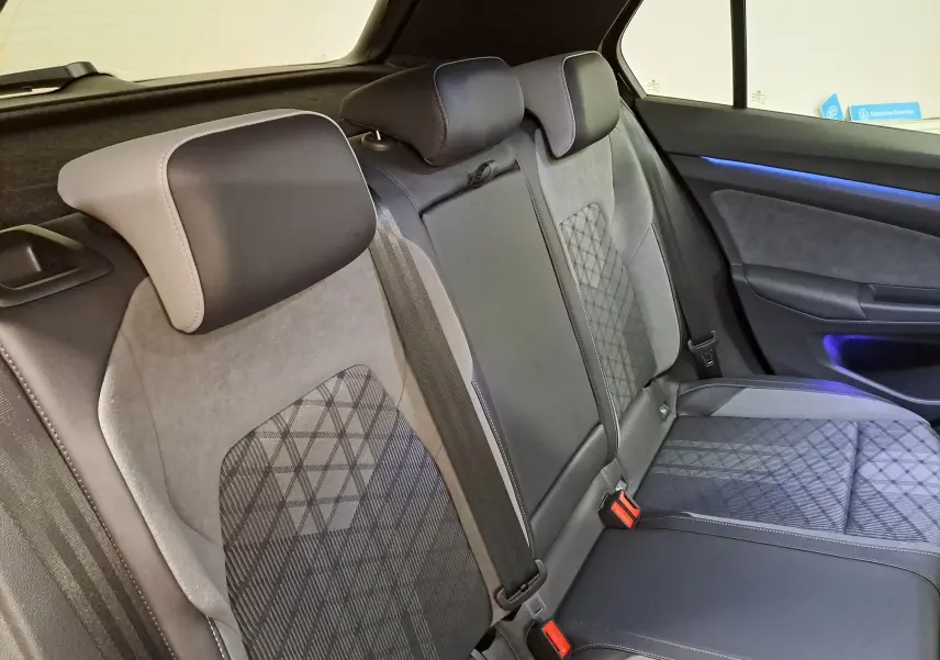 Vue intérieure côté droit des sièges arrière en cuir et tissu gris avec éclairage d'ambiance bleu d'une Volkswagen Golf 2023.