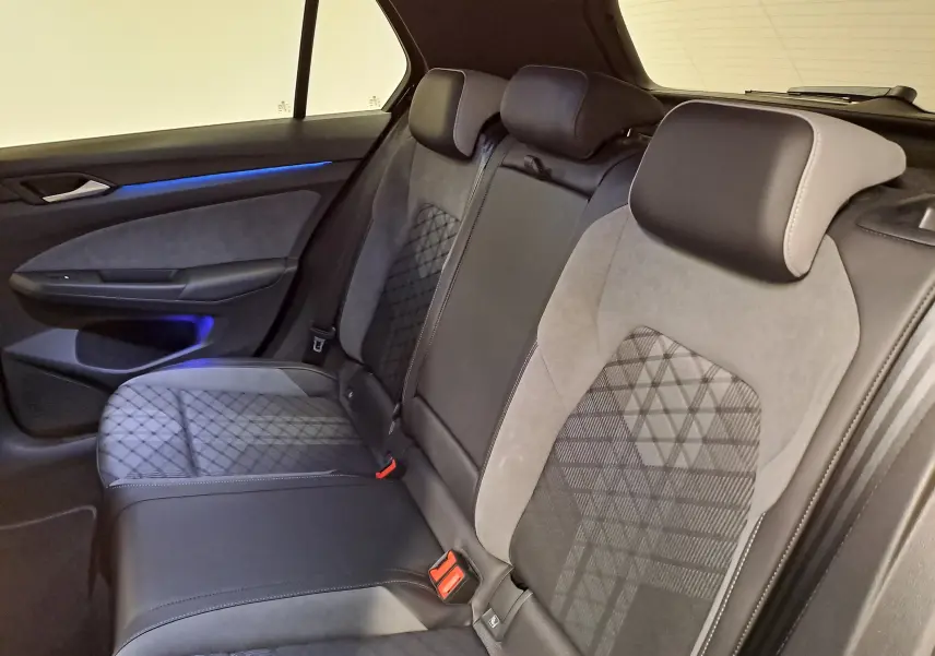 Vue intérieure arrière droite des sièges arrière en tissu et cuir noir avec surpiqûres et éclairage d'ambiance bleu dans une Volkswagen Golf 2023.