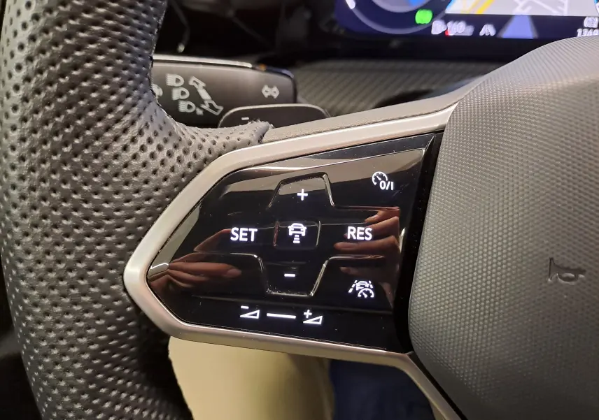 Gros plan sur les commandes noires du volant perforé côté gauche de la Volkswagen Golf 1.5 eTSI 2023.