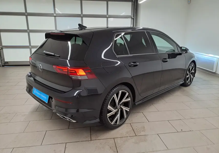 Vue 3/4 arrière droite d'une Volkswagen Golf noire intense nacrée avec jantes alliage distinctives et toit ouvrant en intérieur lumineux.
