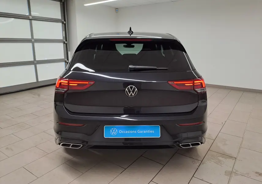 Vue arrière d'une Volkswagen Golf 1.5 eTSI R-Line noire nacrée avec feux LED allumés et double sortie d'échappement chromée.