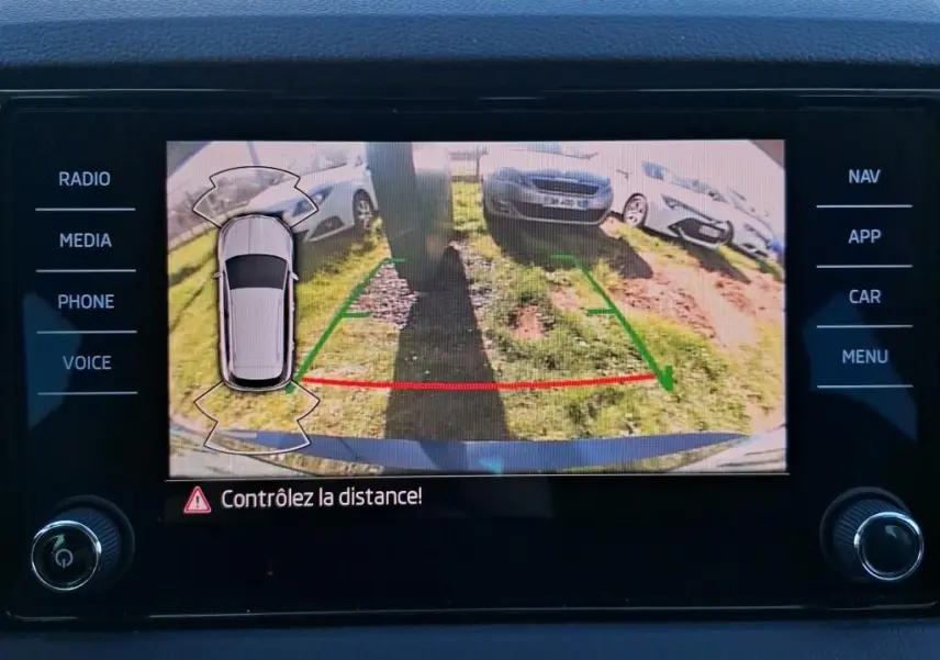 Écran de caméra de recul montrant l'arrière d'une Skoda Karoq bleu avec lignes de guidage vertes et rouges.