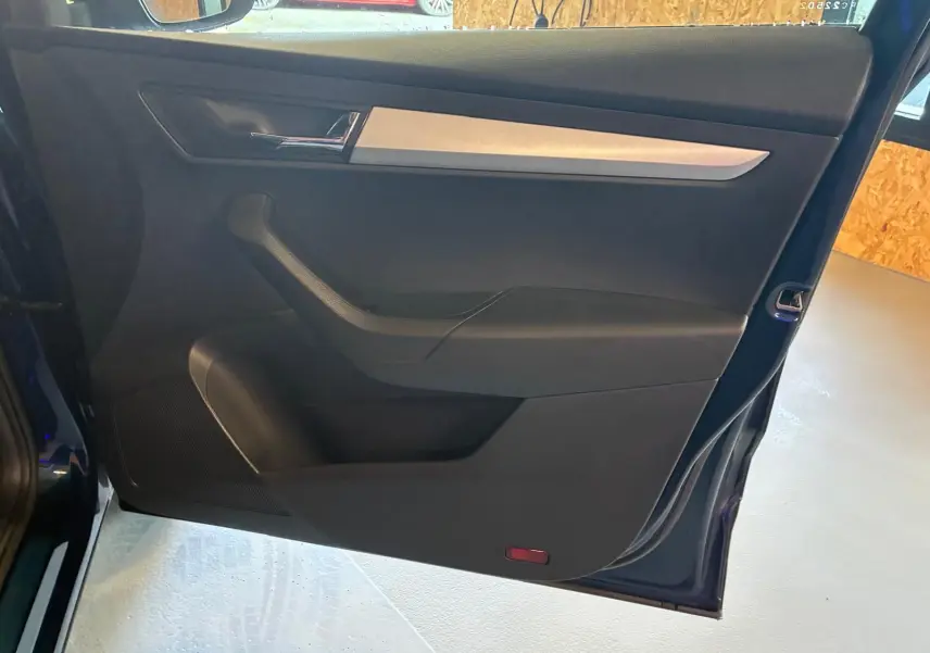 Porte arrière gauche ouverte d’un Skoda Karoq bleu 2023, intérieur noir avec insert décoratif gris clair.