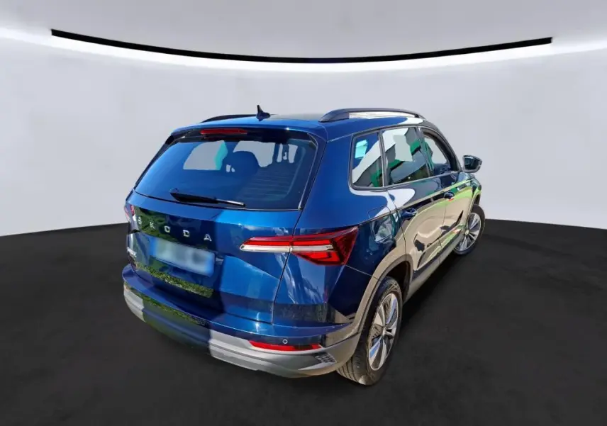 Vue 3/4 arrière droite d'un Skoda Karoq bleu métallisé avec jantes alu 17 pouces et barres de toit noires.