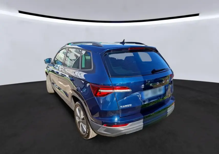 Vue 3/4 arrière droite d'un Skoda Karoq bleu métallisé avec jantes alu 17 pouces et toit avec barres de pavillon noires.