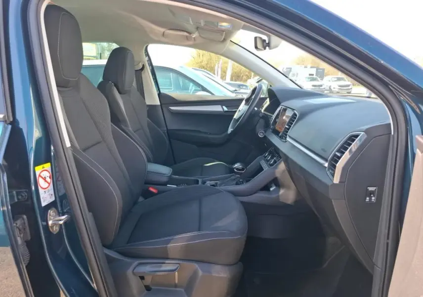 Vue intérieure côté conducteur d'un Skoda Karoq bleu 2026, montrant sièges noirs et tableau de bord moderne.