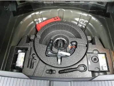 Coffre ouvert du Volkswagen T-Roc 2025 gris foncé, vue plongeante sur le rangement de la roue de secours et outils.