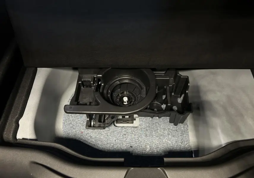 Vue rapprochée du coffre ouvert d’une Fiat 600 noire, montrant le rangement sous plancher avec support d’outils intégré.