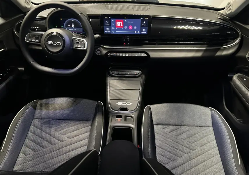 Vue intérieure avant de la Fiat 600 noire, tableau de bord avec écran tactile, volant multifonctions et sellerie bicolore jacquard.
