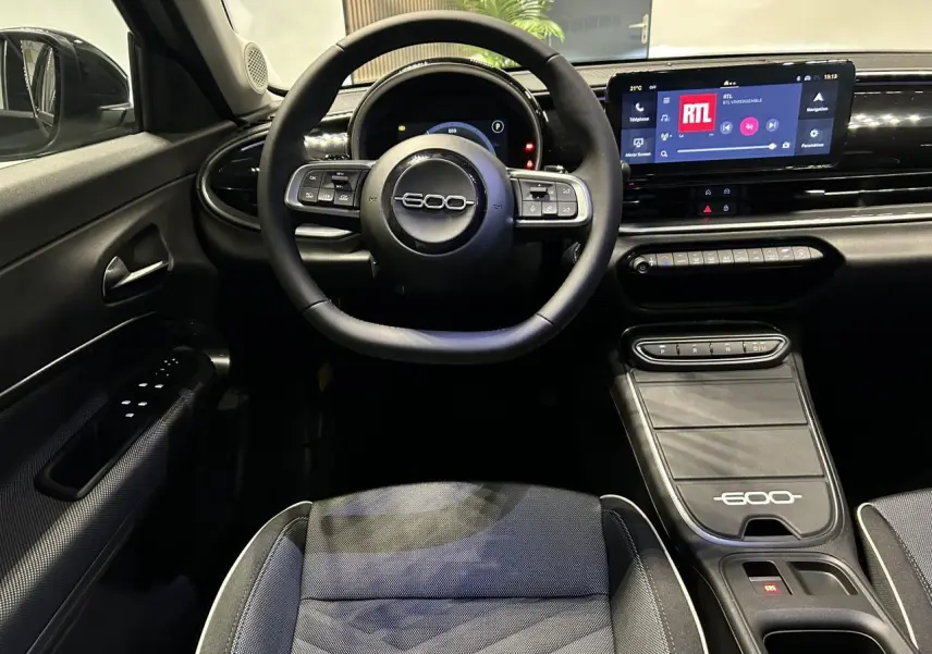 Vue intérieure centrée sur le volant et la console centrale noire du Fiat 600 avec écran tactile et sellerie bicolore.