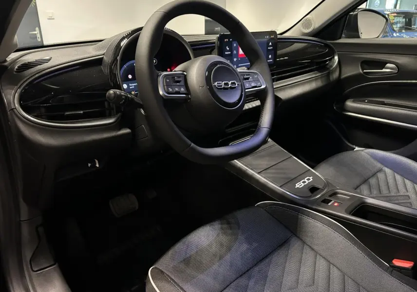 Vue intérieure côté conducteur du Fiat 600 noir, mettant en valeur le volant multifonctions et la console centrale épurée.