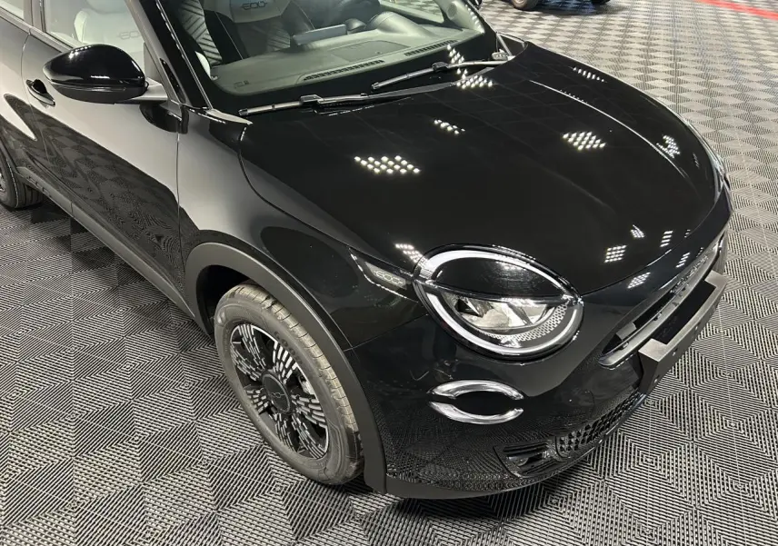 Vue 3/4 avant droit de la Fiat 600 noire avec jantes stylisées et phares ronds distinctifs en intérieur showroom.