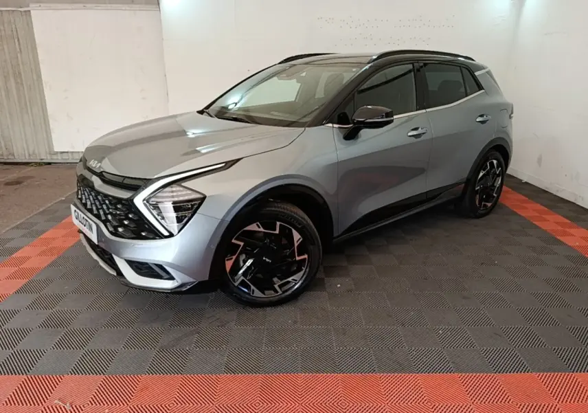 KIA Sportage gris clair en 3/4 avant droit, avec calandre noire et jantes noires à motifs géométriques.
