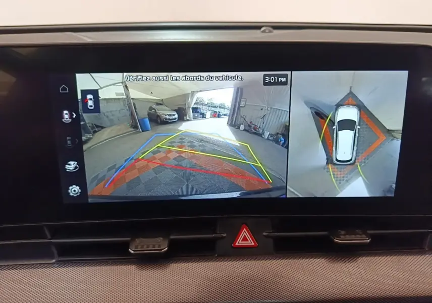 Écran tactile du tableau de bord montrant la caméra 360° et l’aide au stationnement du Kia Sportage gris clair, vue intérieure.