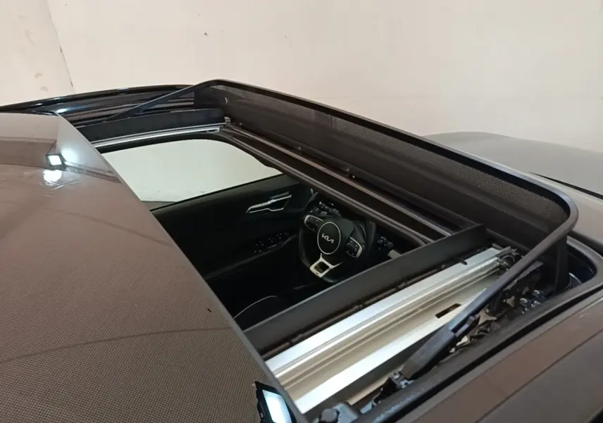 Vue plongeante sur le toit ouvrant ouvert d’un Kia Sportage gris clair, avec aperçu du volant multifonctions intérieur.