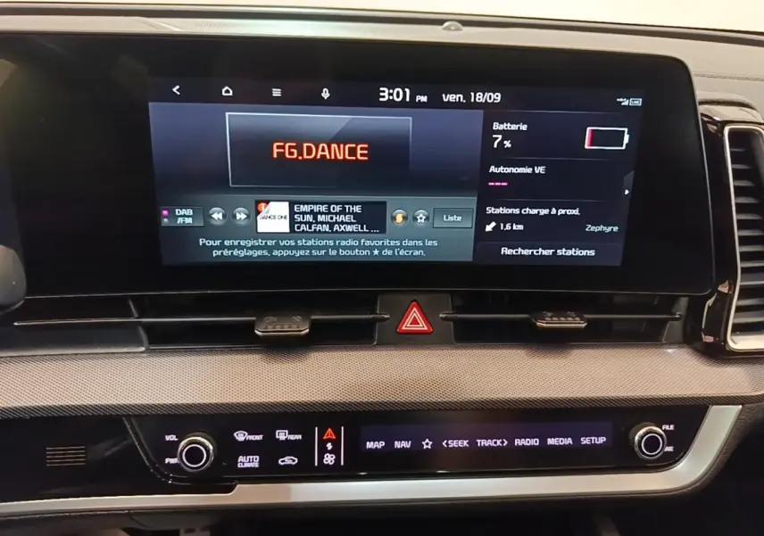 Écran tactile central du tableau de bord du Kia Sportage gris clair, affichant radio et informations batterie.