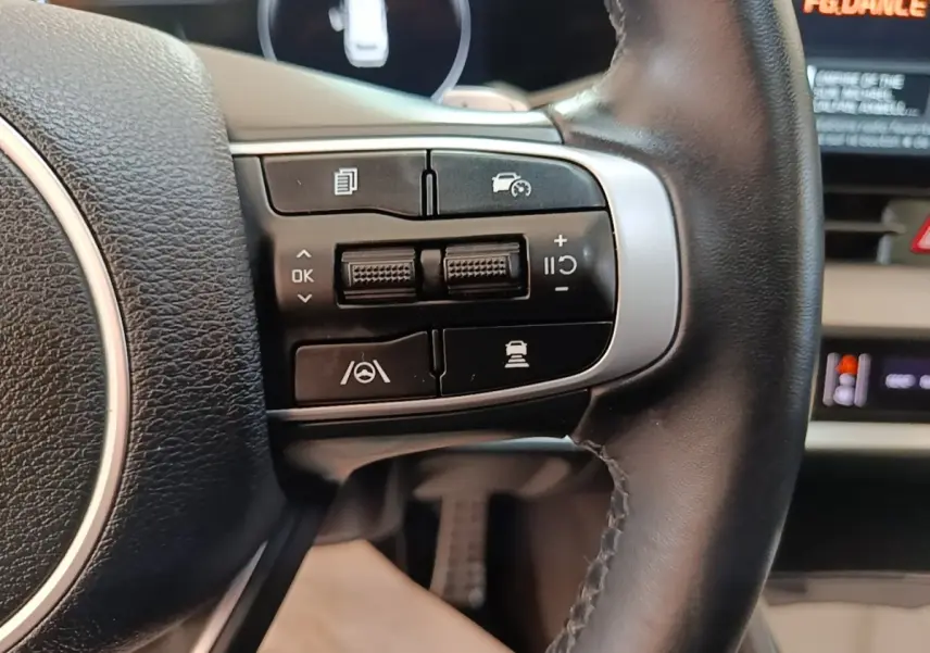 Gros plan sur les commandes du volant cuir noir du Kia Sportage hybride rechargeable, boutons multifonctions visibles.