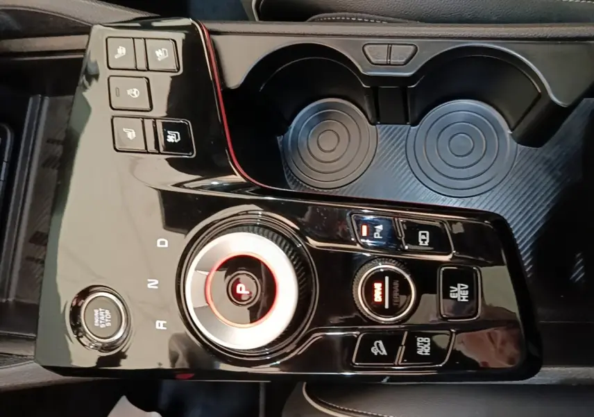 Vue rapprochée de la console centrale noire brillante du Kia Sportage hybride rechargeable avec sélecteur rotatif et boutons multifonctions.