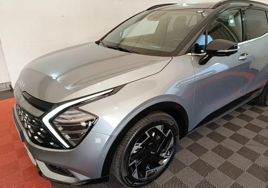Vue 3/4 avant droit d’un KIA Sportage gris clair avec feux LED en forme de C et jantes noires distinctives.