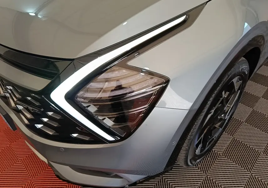Gros plan sur l'avant droit gris clair du Kia Sportage 2022, mettant en valeur son phare LED en forme de boomerang.