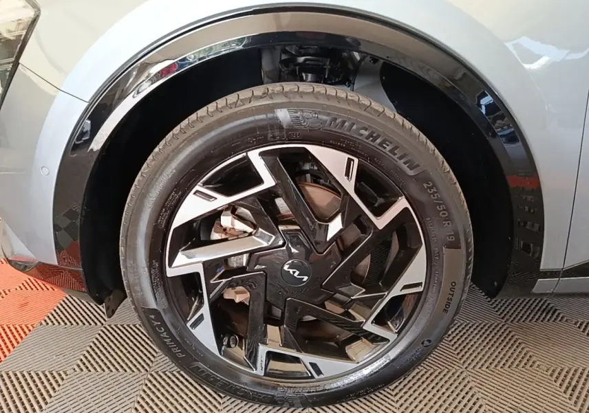 Gros plan sur la roue avant droite du Kia Sportage gris clair 2022 avec jante noire et argentée au design géométrique.