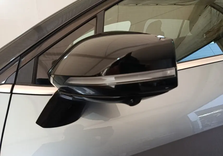 Rétroviseur noir brillant côté gauche du Kia Sportage gris clair, avec fenêtre et partie de la porte visibles.
