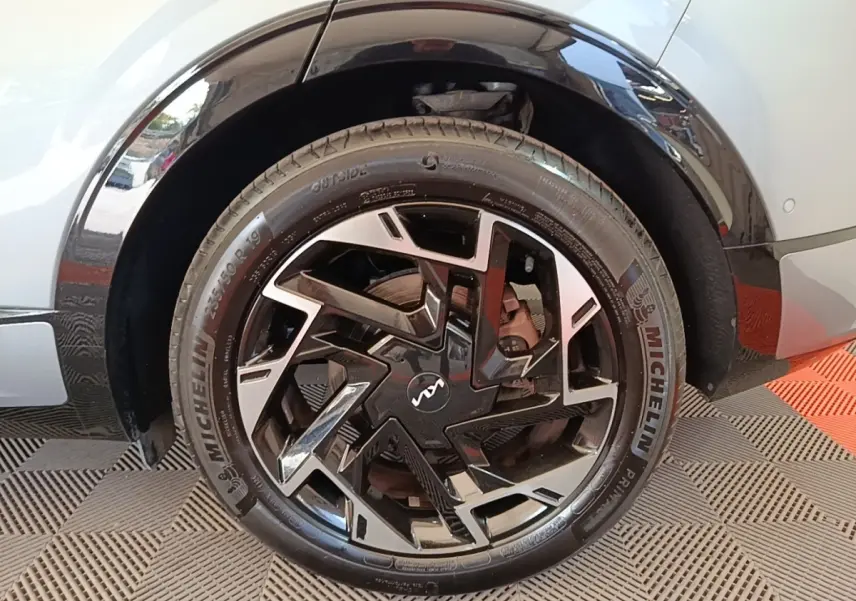 Gros plan sur la roue arrière droite d’un KIA Sportage gris clair avec jante noire et argentée au design géométrique.