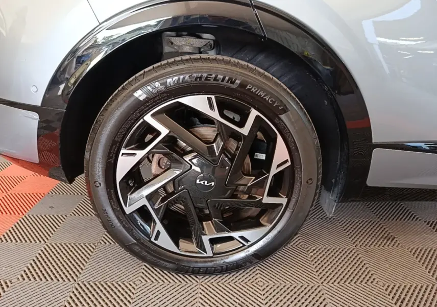 Gros plan sur la roue avant droite d’un KIA Sportage gris clair avec jante noire et argentée au design géométrique.