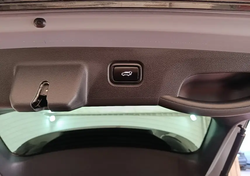 Bouton d'ouverture électrique du coffre sur la partie intérieure du hayon d'un KIA Sportage gris clair, vue rapprochée.
