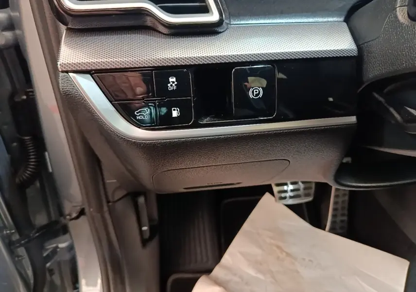 Détail des commandes côté gauche sous le tableau de bord du Kia Sportage gris clair 2022, avec boutons de frein à main et assistance.
