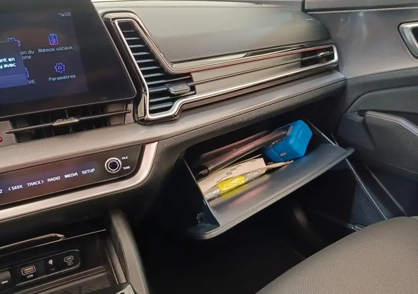 Intérieur côté passager du Kia Sportage 2022, tableau de bord noir avec boîte à gants ouverte contenant divers objets.