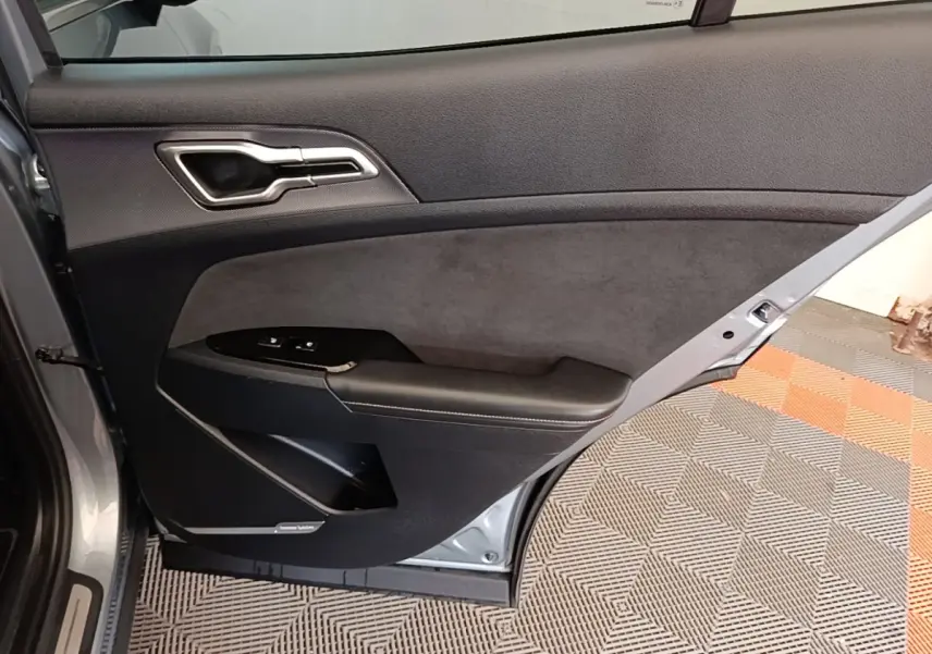 Vue intérieure de la porte arrière gauche gris clair du Kia Sportage 2022 avec garniture noire et commandes de fenêtre.