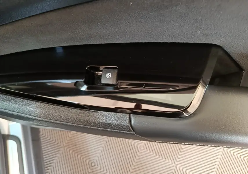 Détail du bouton de commande de lève-vitre sur la porte intérieure d’un Kia Sportage gris clair.