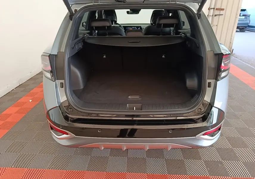 Vue arrière ouverte du coffre d’un KIA Sportage gris clair 2022, avec seuil de chargement noir brillant et intérieur spacieux.