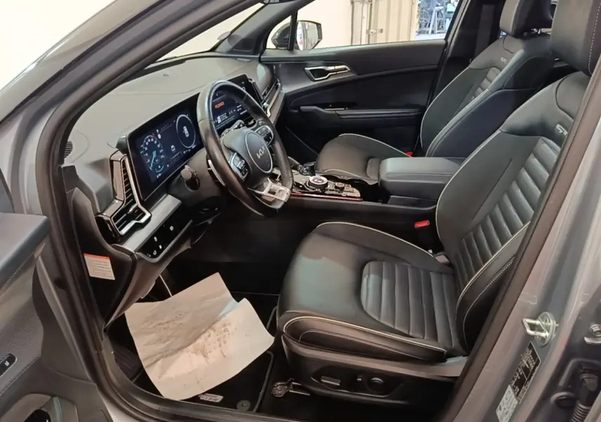 Vue intérieure côté conducteur du Kia Sportage gris clair 2022, avec tableau de bord digital et sièges en cuir noirs GT-Line.