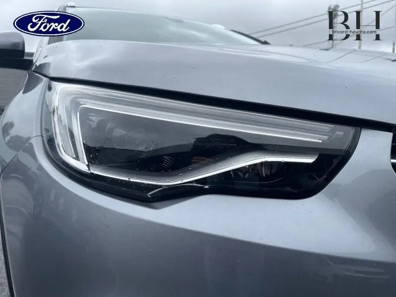 Gros plan sur le phare avant gauche gris Quartz de l’Opel Grandland X avec toit et rétros noirs.