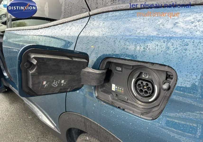 Détail de la trappe de recharge ouverte côté gauche sur Peugeot 3008 hybride rechargeable bleu Celebes métal sous la pluie.
