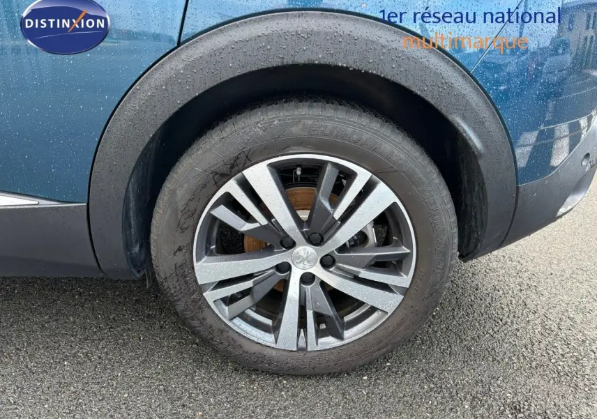 Gros plan sur la roue avant gauche et la jante biton noir et argent du Peugeot 3008 bleu Célèbes métal sous la pluie.
