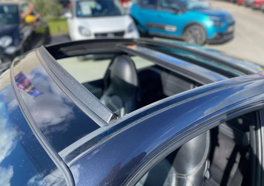 Vue rapprochée du toit coulissant ouvert d’une Porsche 911 Targa gris foncé, avec sellerie cuir noire visible.