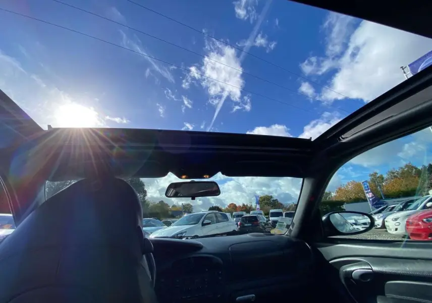 Vue intérieure avant de la Porsche 911 Targa gris foncé, toit ouvert laissant voir le ciel et le pare-brise.