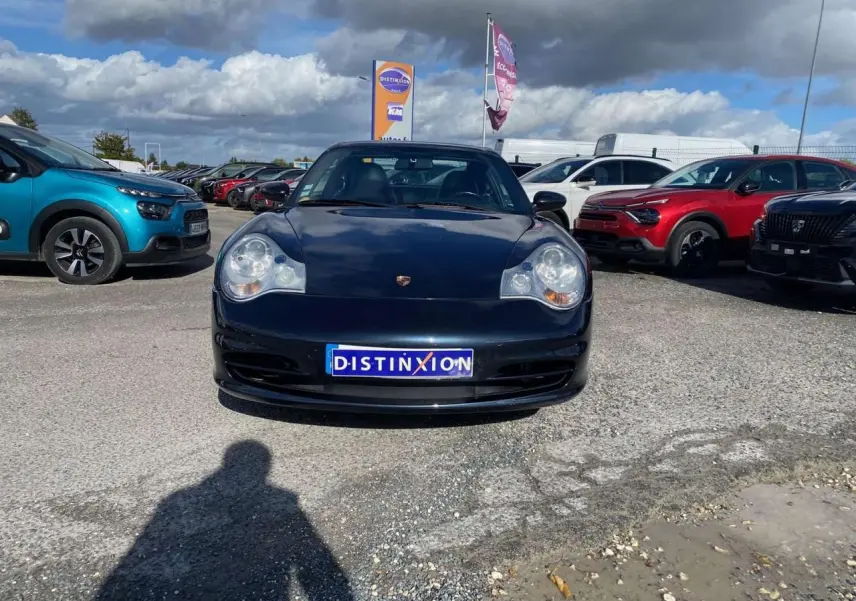 Vue avant d'une Porsche 911 Targa 996 gris foncé stationnée sur un parking sous un ciel nuageux.