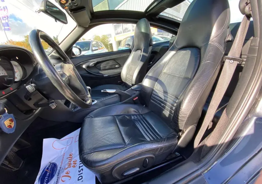 Vue intérieure côté conducteur de la Porsche 911 Targa gris foncé, sièges cuir noirs et levier de vitesse alu-cuir visible.