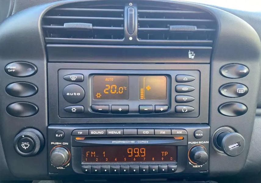 Vue rapprochée du tableau de bord noir de la Porsche 911 Targa 996 gris foncé, montrant la climatisation et la radio d'origine.