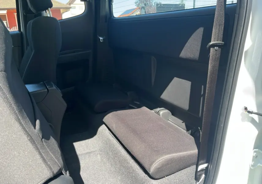 Vue intérieure arrière côté droit du pick-up Isuzu D-MAX 2.2 TD 164 Space Evolution A/T8 en blanc Splash, sièges arrière rabattus.