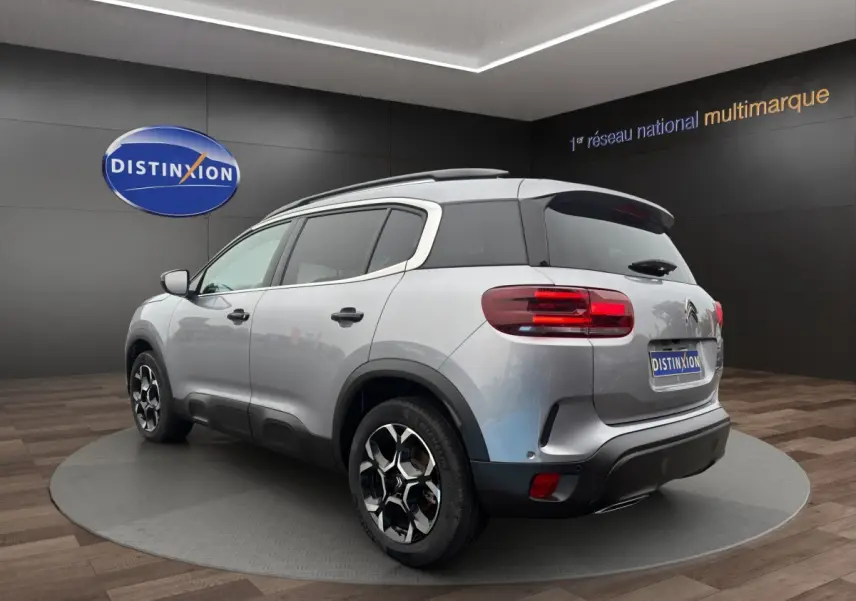 Vue 3/4 arrière droite du Citroën C5 Aircross hybride gris clair avec jantes noires et toit noir en showroom.