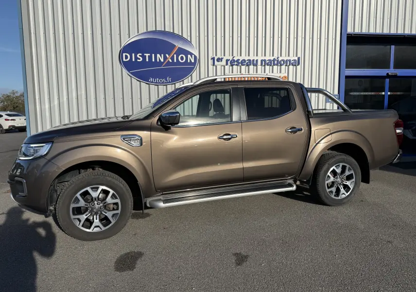 Renault Alaskan brun 2018 en 3/4 avant droit, avec calandre chromée et phares LED visibles, stationné devant un bâtiment.