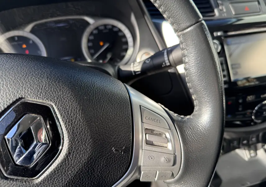 Gros plan sur le volant en cuir noir du Renault Alaskan 2018, avec commandes intégrées et tableau de bord flou en arrière-plan.